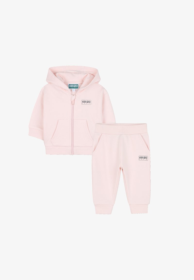 Giacca con cappuccio in rosa chiaro con zip abbinata ai pantaloni. Tessuto morbido, polsini a costine, tasche frontali e etichetta del logo su entrambi i pezzi. Design semplice.