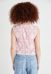 Haut sans manches rose avec un dos en dentelle présentant des motifs circulaires, associé à un jean taille haute bleu clair et d'une texture lisse.