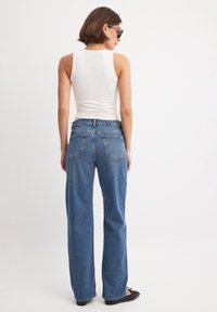 Korke waistline'iga sinised denim teksad lõdvema istuvusega, viie taskuga, tagumise õmbluse detailiga, kombineeritud hästi istuva valge tank-särgiga.