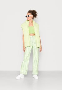 Colete puffer verde-lima com design sem mangas, combinado com um top cropped a condizer e calças largas estampadas com linhas onduladas. Ténis brancos.