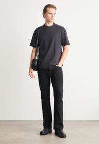 Camiseta de algodón negra de manga corta y corte relajado, combinada con jeans negros de pierna recta y botas negras, accessorios con un bolso pequeño.