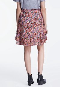 Jupe à motif floral avec des teintes vives de rouge, rose et vert ; design en couches et fluide ; tissu léger ; portée avec des bottines noires.