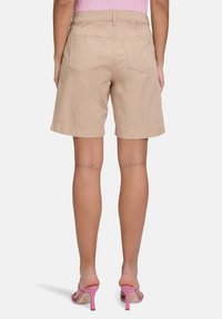 Shorts en coton beige avec une coupe décontractée, ourlet retroussé et poches arrière doubles, présentés de dos sur un fond uni.