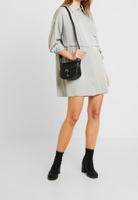 Ljusgrön knapp-up klänning med insydd midja, i kombination med en liten svart crossbody-väska och svarta ankelstövlar. Slät tygtextur.