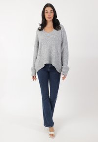 Grau gestrickter Pullover mit V-Ausschnitt und gerippten Bündchen, kombiniert mit blauen Schlagjeans. Die weiche Textur und der lockere Schnitt betonen den Komfort.