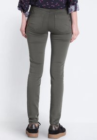 Jeans skinny de color verde oliva con una textura suave y tres bolsillos en la parte trasera, combinados con zapatillas negras que tienen un acento metálico.