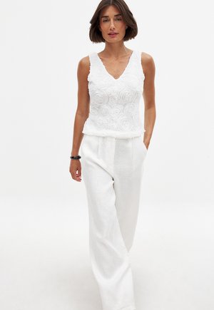 White sleeveless top with textured rose patterns and a V-neck, paired with loose-fitting white linen trousers.