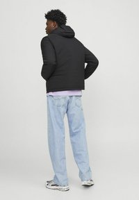 Black hooded puffer jacket made of lightweight fabric, paired with light blue baggy jeans and multi-colored sneakers.