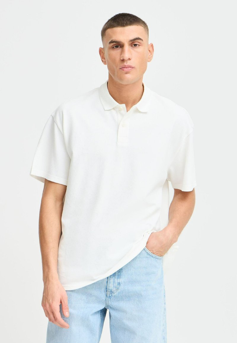 Hvit polo skjorte med avslappet passform, med klassisk krage, korte ermer og subtil tekstur. Kombinert med lyseblå jeans.
