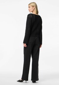 Svart stickad tröja med långa ärmar och ribbad textur, kombinerad med svarta vida jeans och spetsiga klackskor.