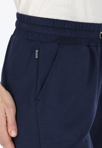 Navyblauwe joggingbroek van zachte stof, voorzien van een elastische tailleband, zijzakken en een klein "SEASIDE" label aan de voorkant.