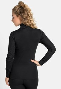 Svart langermet turtleneck topp, laget av elastisk stoff, med tettsittende design og glatt tekstur, med en lett buet hem i bunnen.