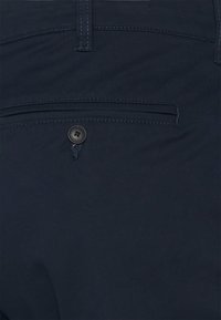 Pantaloni blu navy con una texture liscia, dotati di una tasca posteriore e di un bottone nero. Taglio dritto con dettagli di cucitura minimi.