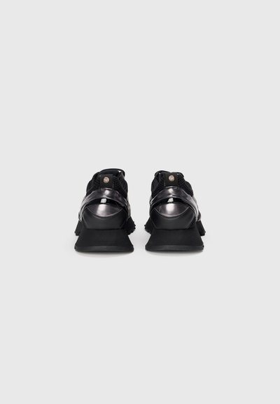 Schwarze Sneaker mit einem strukturierten Mesh-Obermaterial, glänzenden Lack-Akzenten, einem gepolsterten Schaft und einer dicken schwarzen Sohle. Verfügt über ein kreisförmiges Logo auf der Rückseite.