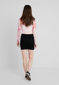 Haut à manches longues avec effet tie-dye en rose et blanc, associé à une mini-jupe en jean noire. La tenue présente une coupe ajustée et des baskets décontractées.