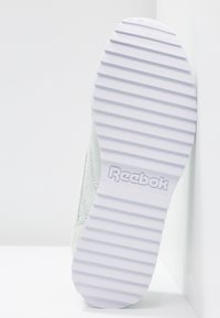 Semelle de chaussure blanche Reebok avec des rainures horizontales et le logo Reebok embossé au centre, sur un fond blanc uni.