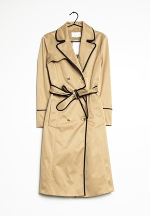 Trench-coat beige avec bordure noire, boutons croisés, taille ceinturée et poches à rabat, suspendu à un cintre noir sur fond blanc.