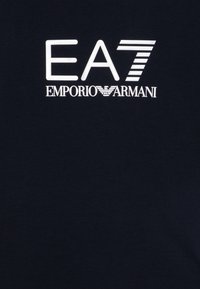 Tamsiai mėlynas medvilninis marškinėliai su balta spauda "EA7" ir "EMPORIO ARMANI", pasižymintys moderniu, minimalizmo stiliumi.