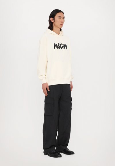 Felpa crema con logo "MSGM" nero, tasca frontale e cordoncino. Abbinata a pantaloni cargo neri con più tasche e una vestibilità rilassata.