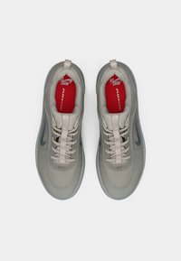 Par tenisica Nike Air Zoom u svijetlo bež boji s crvenim ulošcima i bijelim vezicama, prikazanih odozgo na bijeloj pozadini.