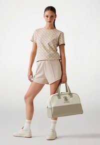 Beežist mustriga puuvillane T-särk, sobivad lühikesed püksid ja beeži-kreemikas logoga spordikott; valged tennised roosade triibuliste sokkidega.