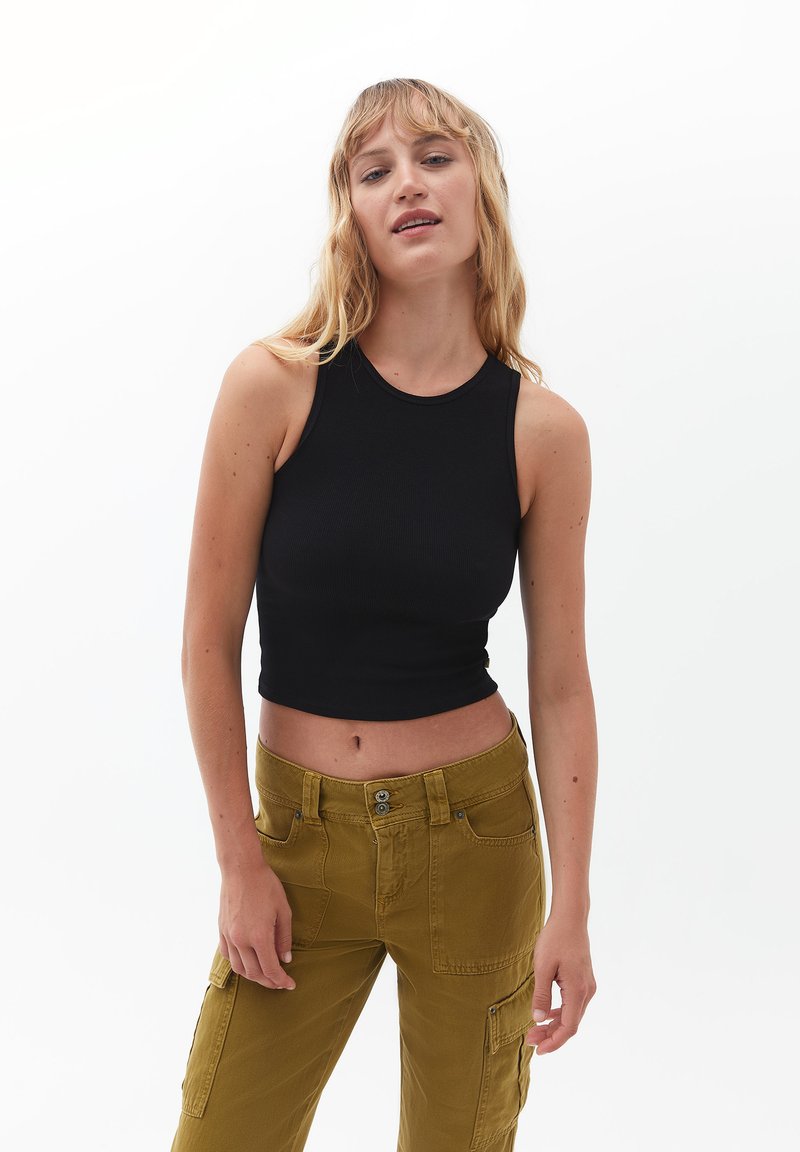 Czarny prążkowany crop top z okrągłym dekoltem, w zestawieniu z oliwkowymi spodniami typu cargo z przednimi kieszeniami i guzikami.