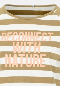 Gros plan sur une chemise rayée beige et blanche avec le texte "RECONNECTEZ-VOUS AVEC LA NATURE" imprimé en rose sur le devant.