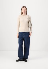 Pulover bej din tricotaje cu guler rotund, asortat cu blugi largi din denim albastru. Accesoriul include o geantă mică de culoare gri deschis.