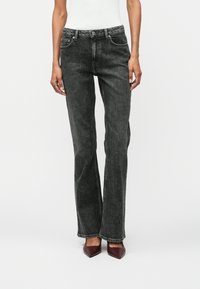 Jeans en denim noir avec une coupe droite, des accents cousus, deux poches avant et une fermeture à bouton classique. Portés avec des talons aiguilles bordeaux.