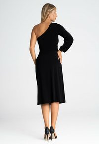 Czarna sukienka na jedno ramię z dopasowaną górą, rozkloszowaną spódnicą do kolan oraz fakturowanym długim rękawem. Uzupełniona czarnymi wysokimi obcasami.