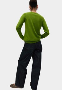 Grüner Strickpullover mit Rundhalsausschnitt, langen Ärmeln und gerippten Bündchen, kombiniert mit dunkelblauen weit geschnittenen Jeans. Weiche Textur, lässiges Design.