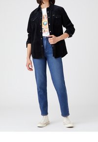 Black corduroy shirt with button front, paired with light blue high-waisted jeans and white sneakers. Graphic t-shirt underneath.