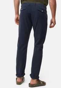 Navy blue cotton trousers with rolled cuffs, two back pockets, and contrasting hardware. Fabric has a smooth texture. Casual design.