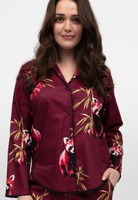 Bordeaux satijnen pyjama-top met prints van rode panda's en bamboe, zwarte knopen en zwarte bies op de manchetten en de kraag.