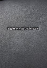 Surface en cuir noir texturé avec un logo en relief de couleur argentée portant la mention "TOMMY HILFIGER".