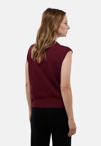 Top sans manches bordeaux avec un design en tricot texturé, un ourlet côtelé et une coupe décontractée, associé à un pantalon noir pour un look monochrome.