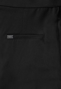 Pantaloni neri realizzati in un tessuto liscio, con una cintura elastica e una tasca discreta con un'etichetta del marchio. Design semplice senza ulteriori accenti.