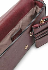 Portafoglio in pelle bordeaux con texture liscia, hardware dorato, tasca con zip e fodera in tessuto a righe. Presenta una chiusura a scatto e scomparti per carte di credito.