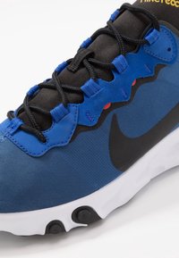 Blå och svart sneaker med mesh- och mockamaterial, med kontrasterande snören, en logotyp och en vit sula med svarta accenter.