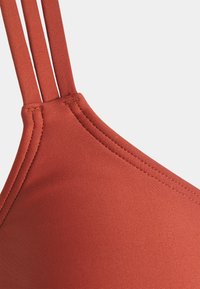 Bikini horná časť v rustikálnej farbe s tenkými dvojitými popruhmi, hladkou textúrou a minimalistickým trojuholníkovým designom. Detaily šitia pri okrajoch.