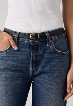 Cinturón de cuero negro con una hebilla metálica dorada, usado sobre jeans de mezclilla azul de tiro alto con costuras naranjas y bordes desgastados.