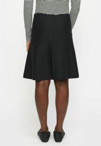 Schwarzer A-Linien-Rock mit glatter Oberfläche, der zum Saum hin ausgestellt ist. Getragen mit einem gestreiften Langarmshirt und schwarzen Ballerinas.