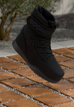 Botte rembourrée noire avec un col haut, présentant un logo bien visible, des lacets et une semelle texturée. Elle flotte au-dessus d'une surface de pierre ornée.