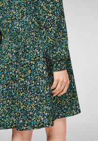 Blommig klänning med svart bas, med mönster i blått, gult och rosa. Tyget är lätt med en lätt glans och korta puffärmar.