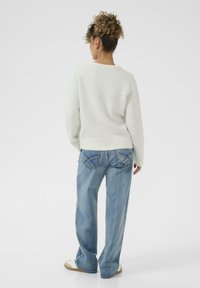 Pull en tricot blanc avec un col rond, associé à un jean bleue clair à jambes larges avec des coutures décoratives et des détails sur les poches.
