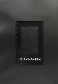 Černá voděodolná taška z látky s obdélníkovým průhledným oknem a bílým vyšitým logem "HELLY HANSEN" ve spodní části.