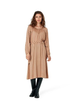 Long-sleeve, blush dress with black polka dots, cinched waist, and relaxed fit, paired with knee-high black boots. Smooth fabric.