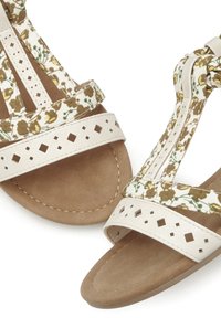 Blumenmuster-Sandalen mit einer tanfarbenen Wildledersohle, cremefarbenen Riemen mit quadratischen Ausschnitten und einem dekorativen Knoten am Knöchelriemen.