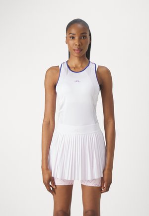 Weißes sportliches Tanktop mit lila Akzenten, kombiniert mit einem plissierten weißen Rock über hellrosa Shorts mit einem Zickzackmuster.