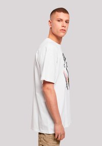 White cotton t-shirt with short sleeves and a loose fit, featuring a graphic design in black and red on the front.